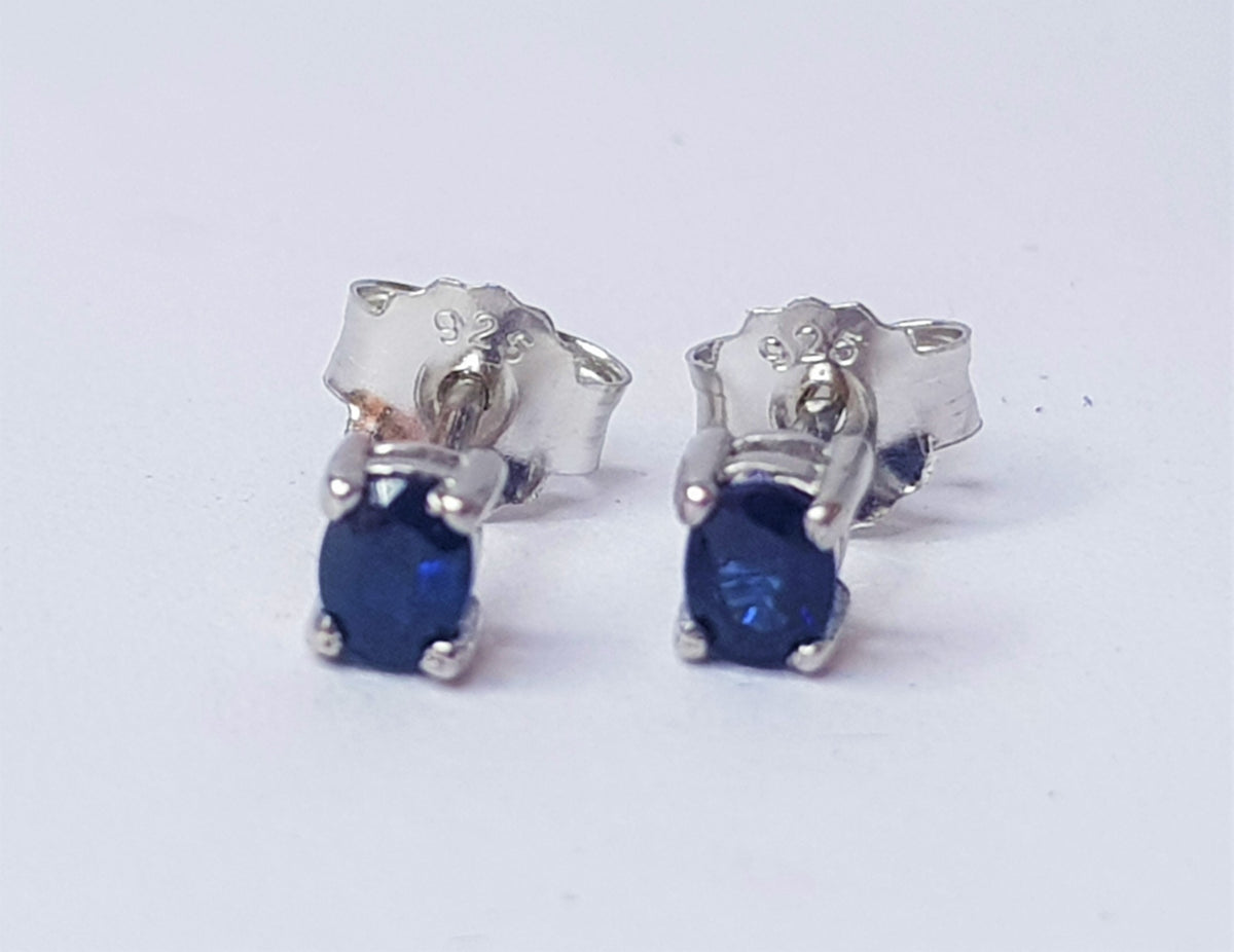 Pair of silver earrings with blue sapphire gemstones on a white background