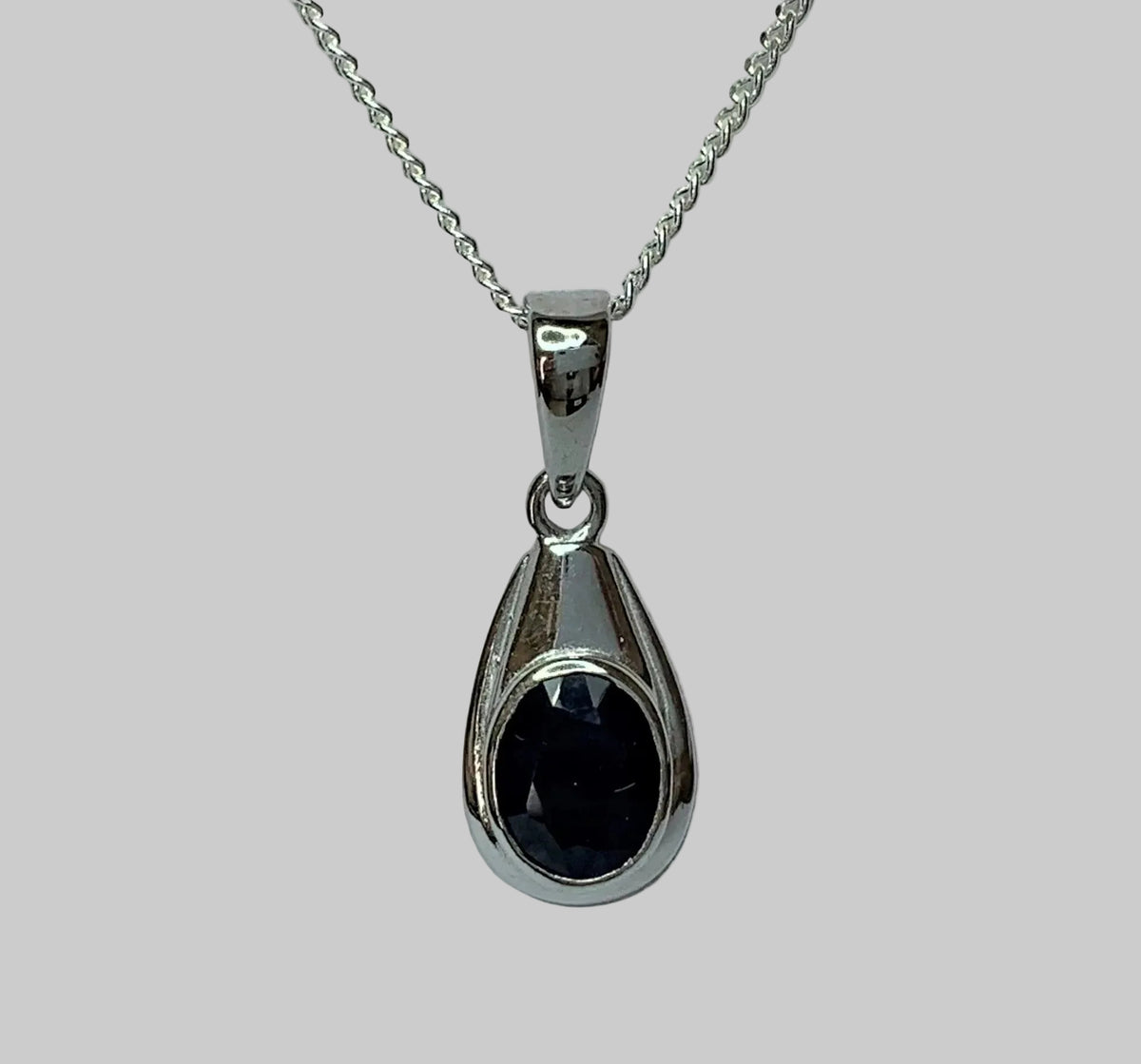 Faceted oval midnight blue sapphire pendant in a bezel sterling silver setting.