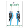 A pair of bird-shaped dangle earrings displayed on a white backing card. The earrings are designed to look like blue and white budgerigars with black speckled wings.