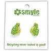 A pair of green frog stud earrings with yellow and orange accents, mounted on a white backing card printed with the brand name 'smyle DESIGNS' and the slogan 'Recycling never looked so good!'.