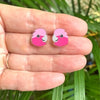 Pink flamingo-shaped earrings held between fingers with a green leafy background
