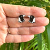Penguin-shaped earrings held between fingers with a natural background