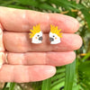 Two small animal earrings held between fingers with a natural background
