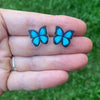 Blue butterfly earrings held between fingers against a green grass background